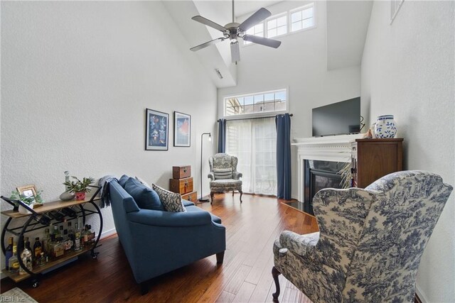 living area featuring ceiling fan, a fireplace, wood finished floors, a high ceiling, and a textured wall