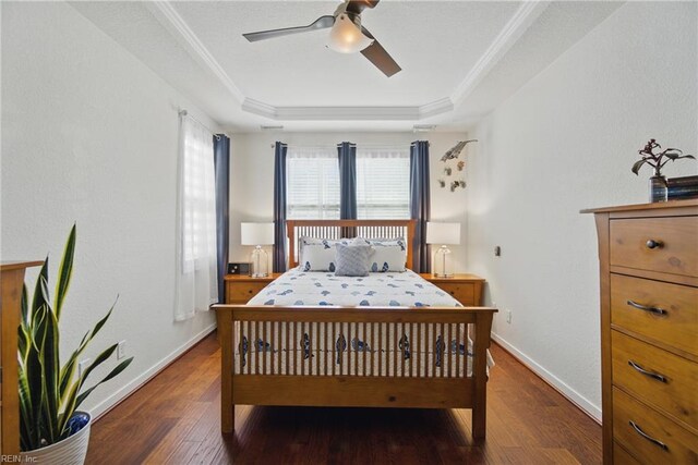 bedroom with ceiling fan, baseboards, wood finished floors, a tray ceiling, and ornamental molding