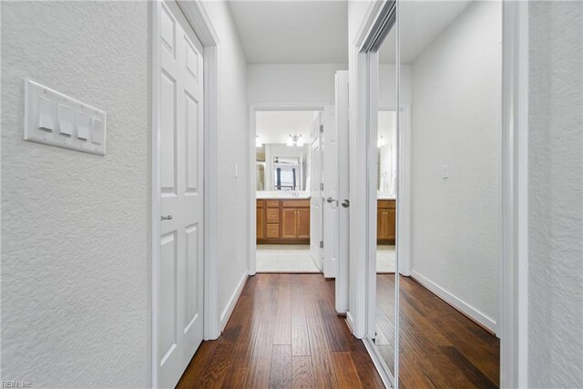 hall with baseboards, a textured wall, and dark wood finished floors