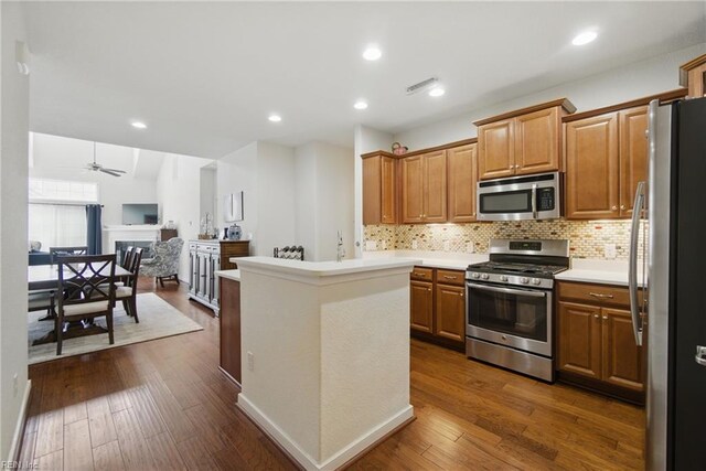 kitchen with backsplash, appliances with stainless steel finishes, light countertops, open floor plan, and dark wood-type flooring