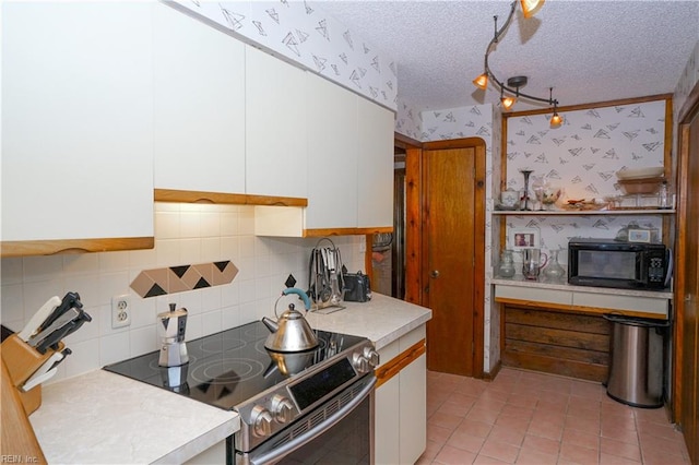 kitchen featuring electric range, black microwave, wallpapered walls, light countertops, and white cabinetry