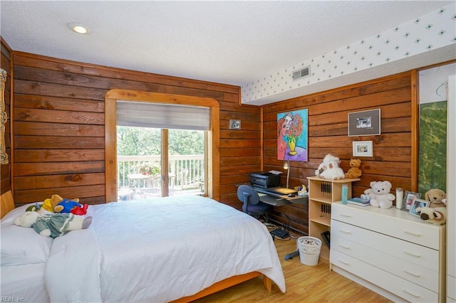 bedroom featuring a textured ceiling, visible vents, wood walls, access to outside, and light wood-style flooring
