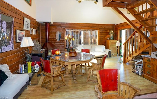 dining room with wood walls, stairs, wood finished floors, and high vaulted ceiling