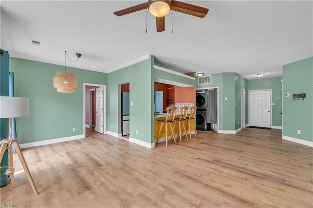 living area with stacked washing maching and dryer, ceiling fan, a textured ceiling, and visible vents