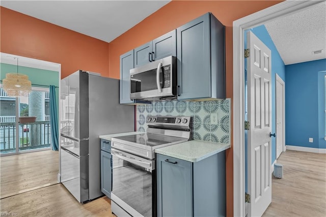 kitchen featuring baseboards, light wood-type flooring, light countertops, tasteful backsplash, and stainless steel appliances
