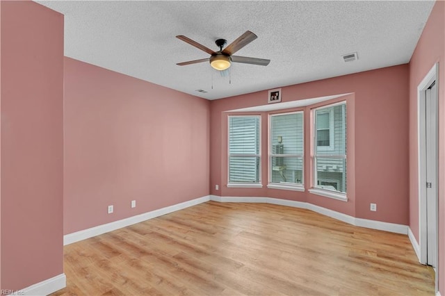 spare room featuring ceiling fan, a textured ceiling, visible vents, baseboards, and light wood-style flooring