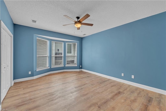 unfurnished room with light wood finished floors, a textured ceiling, a ceiling fan, baseboards, and visible vents