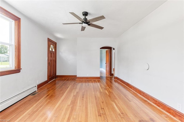 spare room featuring arched walkways, light wood-style flooring, a ceiling fan, baseboards, and a baseboard radiator