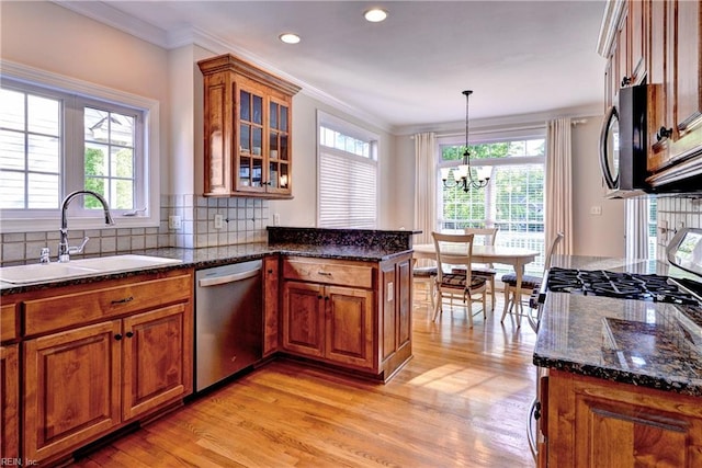 kitchen featuring brown cabinetry, appliances with stainless steel finishes, a sink, a chandelier, and light wood-style floors