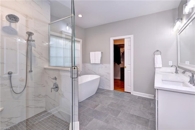 bathroom featuring double vanity, tile walls, a sink, a marble finish shower, and a soaking tub