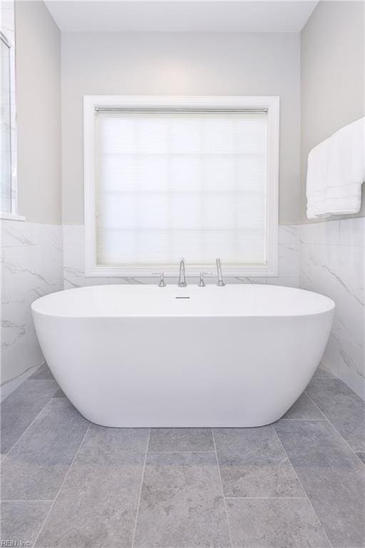 bathroom with wainscoting, a freestanding bath, a healthy amount of sunlight, and tile walls