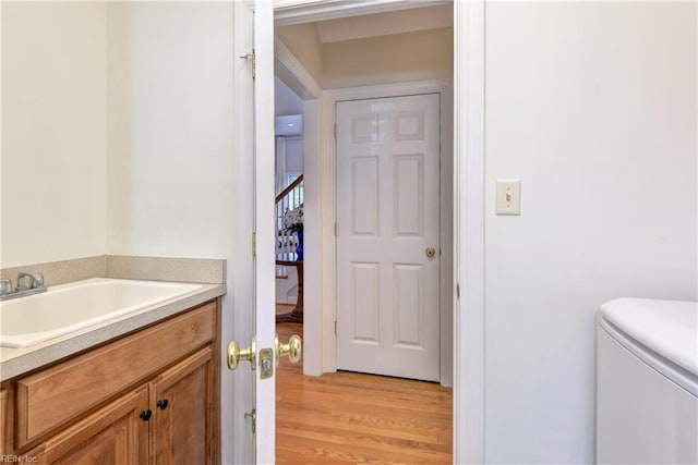 half bathroom with washer / dryer, vanity, toilet, and wood finished floors