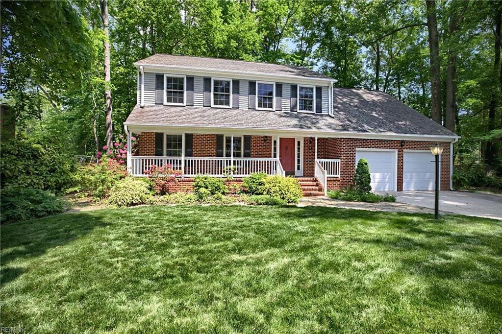 view of front of home featuring an attached garage, a front lawn, brick siding, covered porch, and driveway