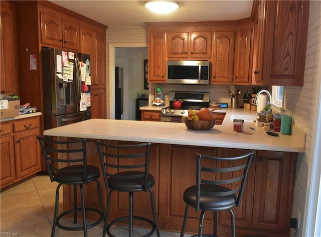 kitchen featuring brown cabinets, appliances with stainless steel finishes, a sink, light countertops, and a peninsula