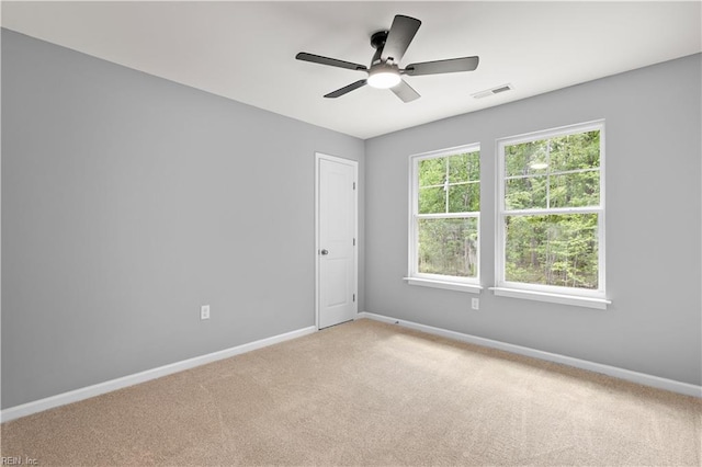 spare room with light colored carpet, baseboards, visible vents, and ceiling fan