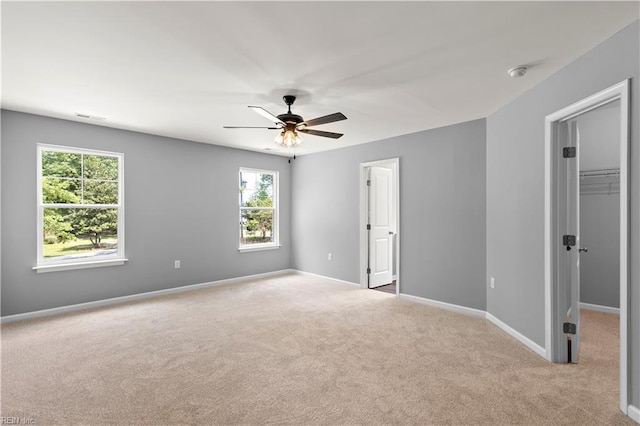 unfurnished bedroom featuring a walk in closet, a ceiling fan, visible vents, baseboards, and carpet