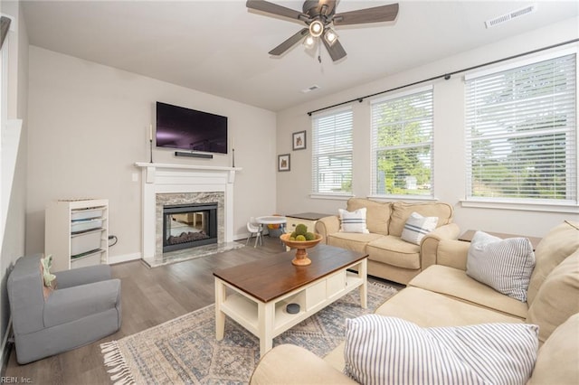 living area featuring a premium fireplace, a ceiling fan, baseboards, wood finished floors, and visible vents