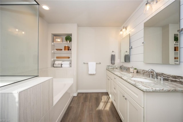 full bathroom featuring double vanity, a garden tub, wood finished floors, a sink, and baseboards