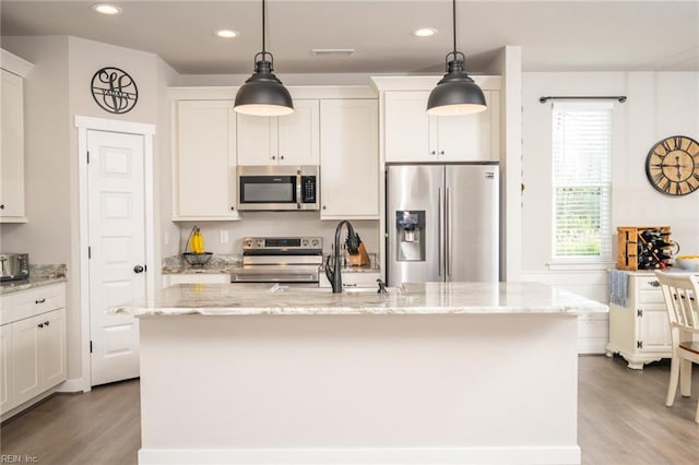 kitchen with a sink, light wood finished floors, a center island with sink, stainless steel appliances, and pendant lighting