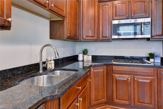kitchen with brown cabinets, appliances with stainless steel finishes, a sink, and dark stone countertops