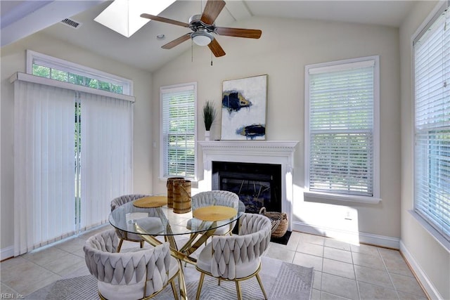 tiled dining space with baseboards, a glass covered fireplace, vaulted ceiling with skylight, and a wealth of natural light