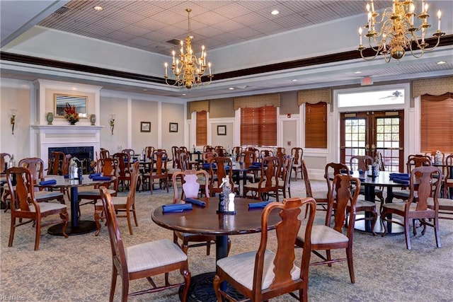 carpeted dining room with an inviting chandelier, ornamental molding, a fireplace, a tray ceiling, and french doors
