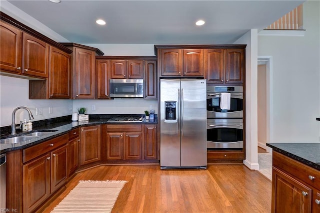 kitchen with a sink, appliances with stainless steel finishes, light wood finished floors, and dark stone counters