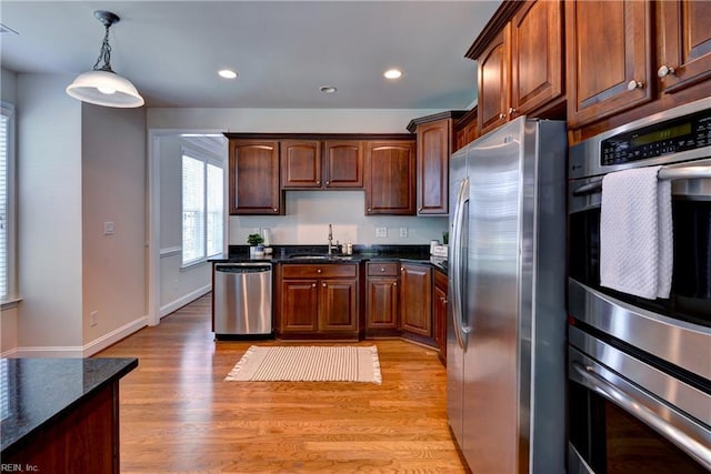 kitchen featuring decorative light fixtures, light wood-type flooring, a sink, baseboards, and stainless steel appliances