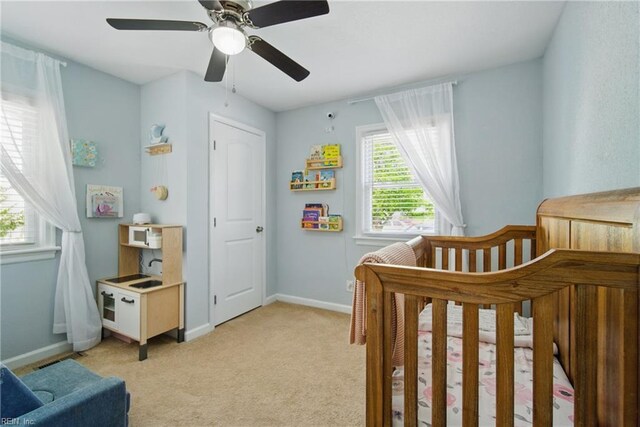 bedroom featuring baseboards, light colored carpet, a crib, and ceiling fan