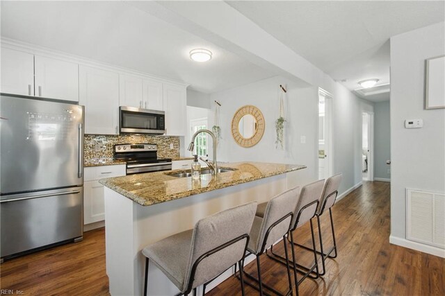 kitchen with light stone countertops, dark wood-style floors, a sink, backsplash, and stainless steel appliances