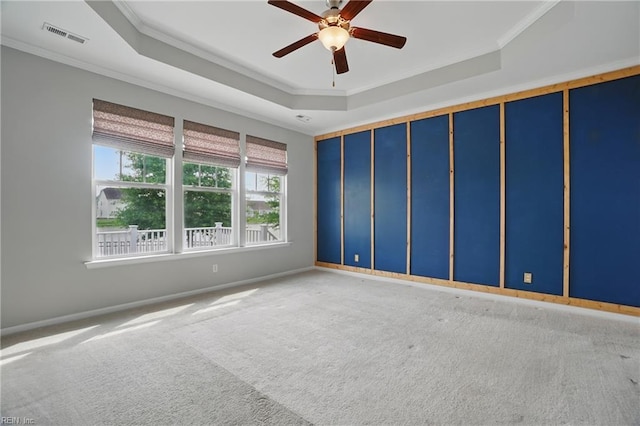 unfurnished room with ceiling fan, a raised ceiling, carpet, visible vents, and ornamental molding
