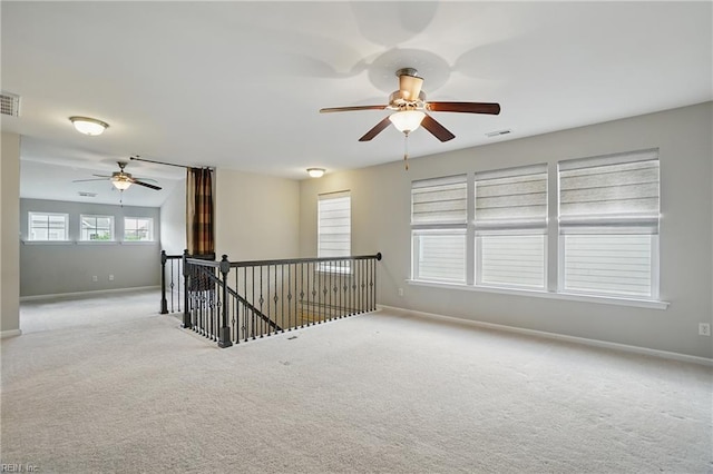carpeted empty room with baseboards, a ceiling fan, and visible vents