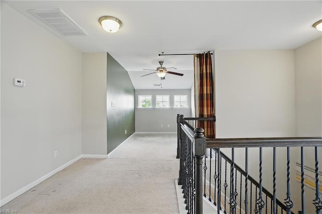 hall with visible vents, baseboards, an upstairs landing, and light colored carpet