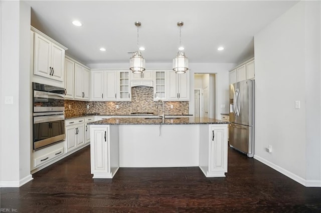 kitchen featuring decorative backsplash, an island with sink, a sink, dark stone countertops, and appliances with stainless steel finishes
