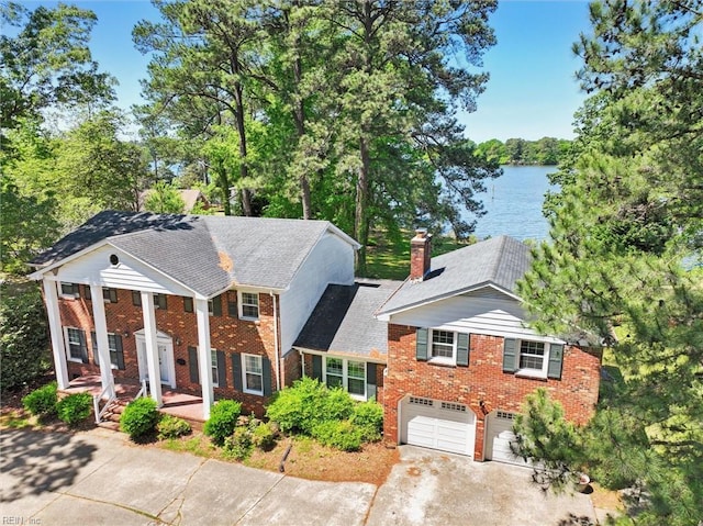 neoclassical / greek revival house featuring a porch, brick siding, concrete driveway, a water view, and an attached garage