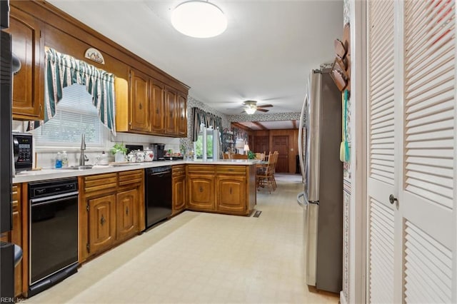 kitchen featuring a sink, light countertops, black dishwasher, a peninsula, and freestanding refrigerator
