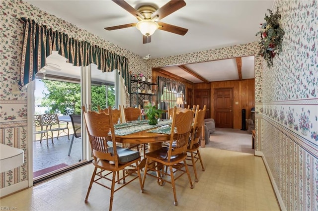 dining room featuring wooden walls, wallpapered walls, ceiling fan, and beam ceiling