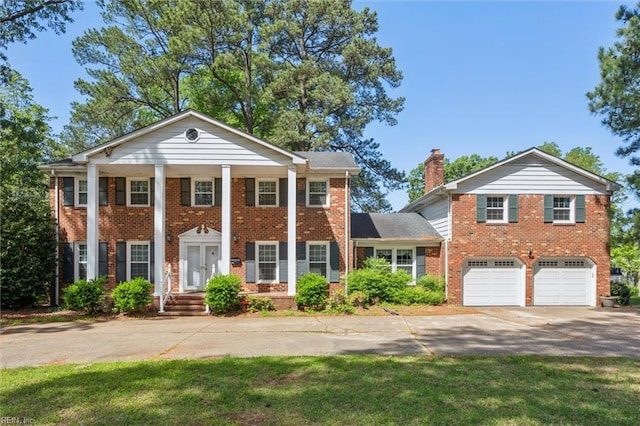 greek revival house featuring an attached garage, a chimney, concrete driveway, and brick siding