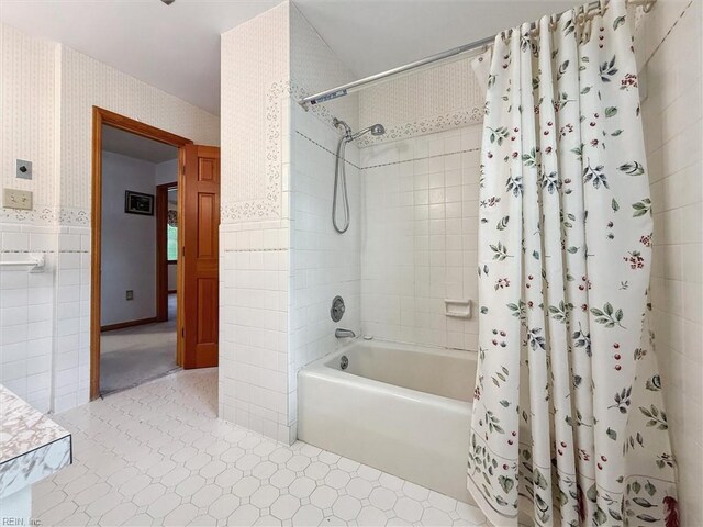 bathroom featuring tile walls, wallpapered walls, a wainscoted wall, tile patterned floors, and shower / tub combo