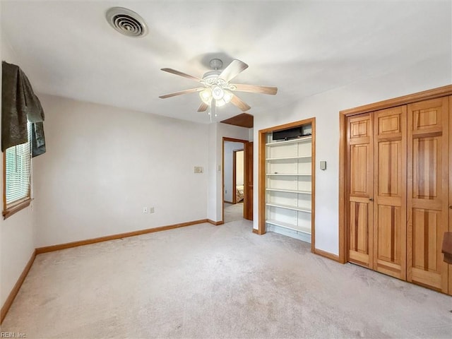unfurnished bedroom featuring visible vents, multiple closets, baseboards, light colored carpet, and a ceiling fan