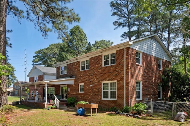 back of property featuring a lawn, a gate, fence, and brick siding