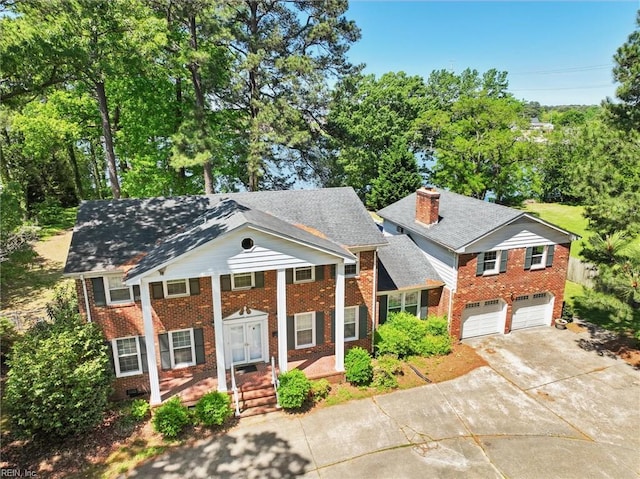 greek revival inspired property featuring a chimney, concrete driveway, a porch, and brick siding