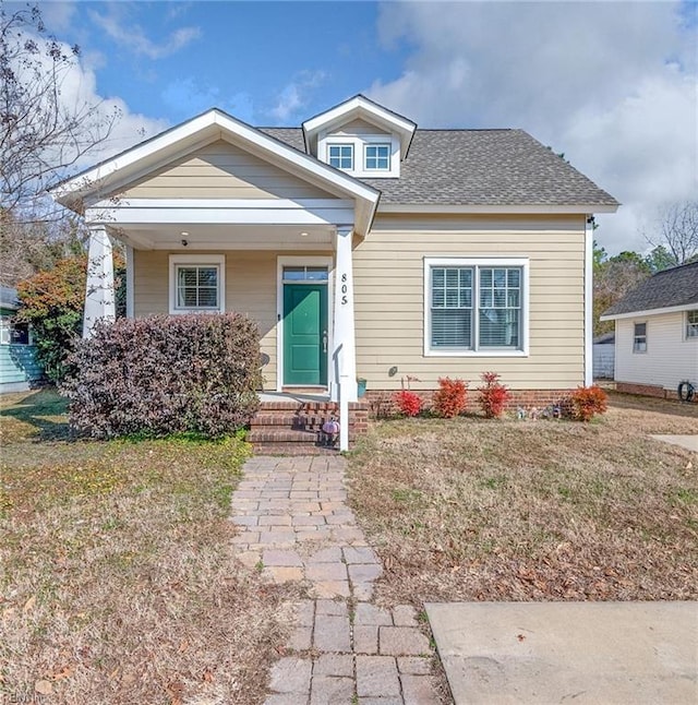bungalow-style home with a porch, a front lawn, and roof with shingles