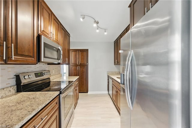 kitchen featuring light stone countertops, baseboards, light wood-type flooring, appliances with stainless steel finishes, and backsplash