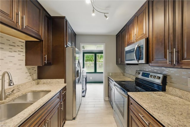 kitchen with dark brown cabinets, light stone countertops, tasteful backsplash, a sink, and appliances with stainless steel finishes
