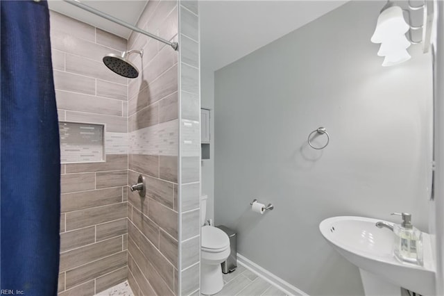 bathroom with baseboards, a sink, a tile shower, and toilet
