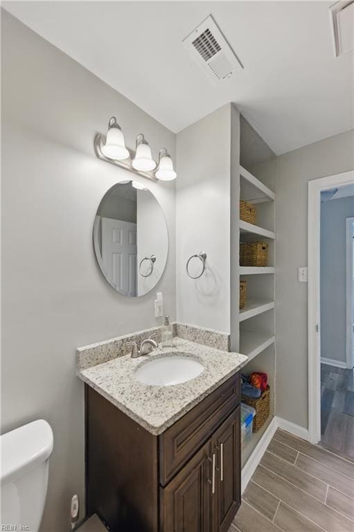 half bath featuring visible vents, wood finished floors, vanity, baseboards, and toilet