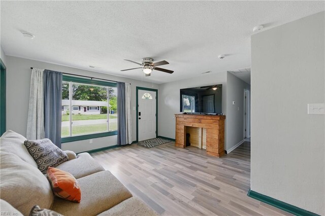 living area with light wood-style floors, baseboards, a ceiling fan, and a textured ceiling