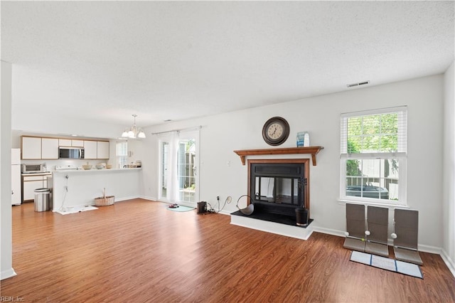 unfurnished living room featuring wood finished floors, plenty of natural light, a glass covered fireplace, baseboards, and a textured ceiling