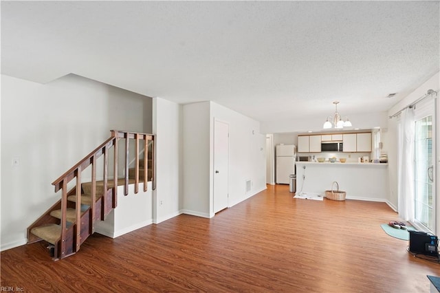 unfurnished living room with a chandelier, wood finished floors, stairs, baseboards, and a textured ceiling